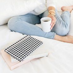 a woman is sitting on her bed holding a cup of coffee and some napkins