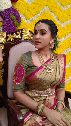 a woman sitting in a chair wearing a gold and pink sari with jewelry on her neck