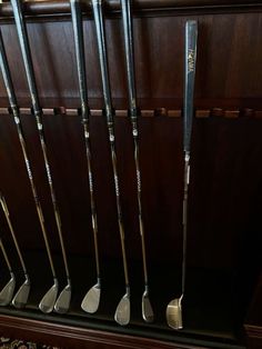 several golf clubs are lined up on a shelf in a room with wood paneling