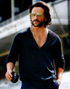 a man with long hair and sunglasses holding a skateboard in his hand while walking down the street