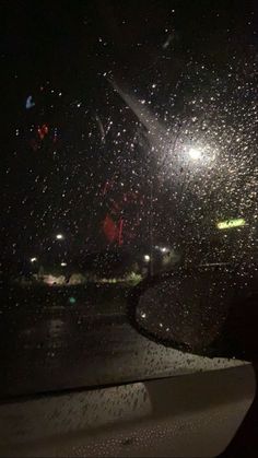 rain is falling down on the windshield of a car at night with street lights in the background