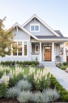 a gray house with white trim and flowers in the front yard