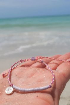 a person's hand holding a beaded bracelet on the beach