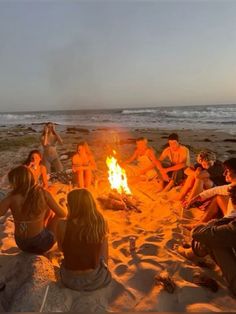 a group of people sitting around a campfire on the beach