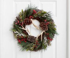 a wreath with antlers, pine cones and berries hanging on a white front door