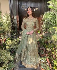 a woman standing in front of some plants wearing a green and gold lehenga