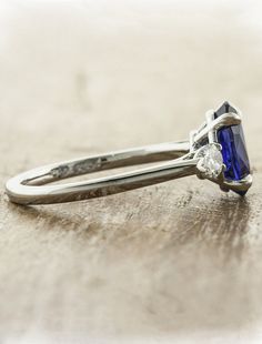 a blue diamond ring sitting on top of a wooden table next to a pair of scissors