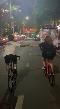 two people riding bikes down the street at night with their arms outstretched to each other