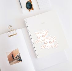 an open notebook sitting on top of a white table next to a pair of sunglasses