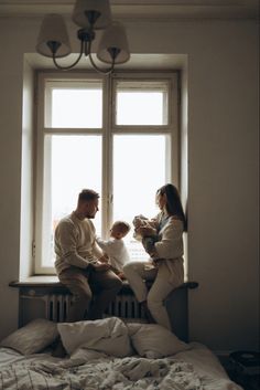 a man, woman and child sitting on a window sill in front of a bed