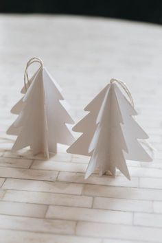 two white paper christmas trees sitting on top of a tile floor next to each other