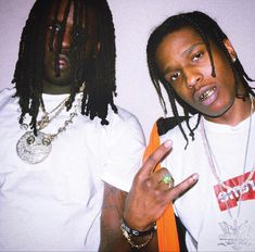 two young men with dreadlocks standing next to each other, one pointing at the camera