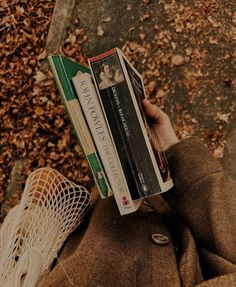 a person holding two books in their hands while standing on the ground with leaves around them