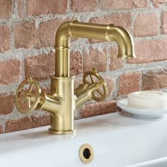 a gold faucet sitting on top of a white sink next to a brick wall