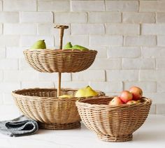 three wicker baskets with apples and pears in them on a white countertop