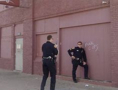 two police officers standing in front of a garage door with graffiti on the wall behind them