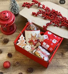 a red box filled with assorted christmas items on top of a wooden table next to pine cones