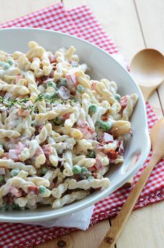 a white bowl filled with pasta salad on top of a red and white checkered table cloth