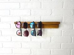 five pairs of sunglasses are hanging on a wooden rack against a white brick wall,