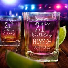 two personalized glasses sitting on top of a wooden table next to lime wedges