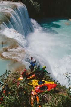 two kayakers sit on the edge of a cliff next to a large waterfall