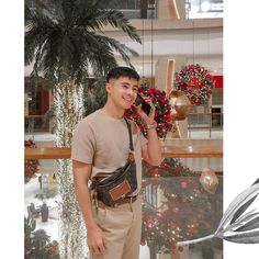 a man standing in front of a christmas tree talking on a cell phone while holding a purse