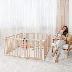 a woman sitting in a chair next to a baby crib and reading a book