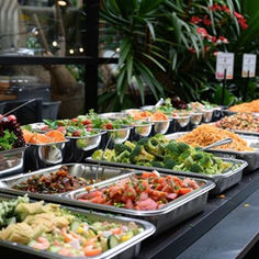 many trays of food are lined up on a table in front of some plants