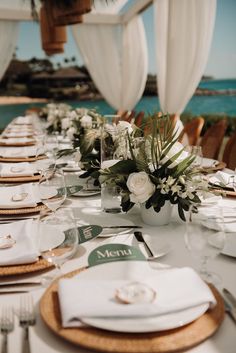 the table is set with white flowers and place settings for an elegant dinner at the beach