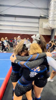 two women in blue and black uniforms hugging each other on a wrestling mat while people watch from the sidelines