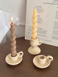 three candles sitting on top of a wooden table next to a cup and saucer