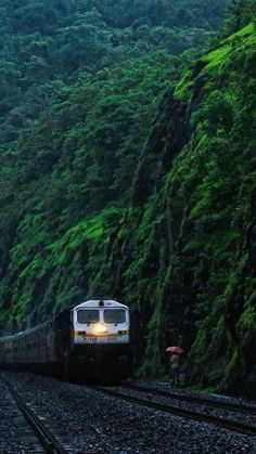 a train traveling down tracks next to a lush green mountain