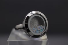 "This unisex customizable cremation ash locket ring is new to our collection of fill-at-home cremation pieces. Your purchase includes the silver ring and opal color of your choice and does not require mailing the ashes. It is composed of sturdy glass and stainless steel (hypoallergenic, scratch/tarnish resistant). The circle is 20mm across with the window being 12mm. The sturdy band is 4mm wide. The ring ships with your choice of synthetic crushed opal (over 90 colors to choose from). After adding ashes, sand, dried funeral flowers, etc., simply screw the front portion in place. For added security, we recommend adding a drop or two of superglue once you've added your inclusions. For your convenience, you have the option to purchase a single-use tube of superglue via the drop-down menu. All Ashes Ring 1stdibs, Ashes Jewelry Cremation Spirit Piece Memorials, Ashes In Resin Sterling Silver, Resin Necklace With Ashes, Rings For Ashes Sterling Silver, Memorial Jewelry Ashes Men, Ashes Ring Gold, Ashes In Resin Ring, Personalized Memorial Ring Jewelry