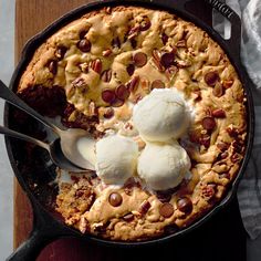 a skillet filled with ice cream and chocolate chip cookie dessert on top of a wooden table