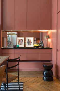 a room with pink walls and wooden floors, two chairs are in the foreground