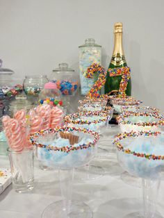 a table topped with glasses filled with cupcakes next to bottles of champagne and candy