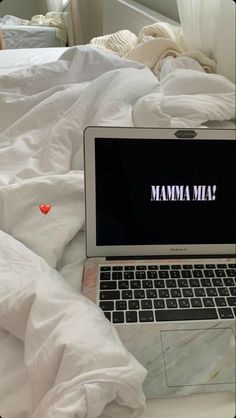 an open laptop computer sitting on top of a bed covered in white sheets and blankets