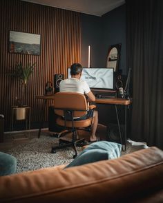 a man sitting at a desk in front of a computer on top of a wooden table