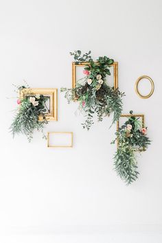 three gold frames with flowers and greenery hanging from them on the wall in an empty room