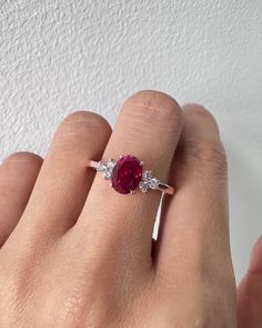 a woman's hand holding a ring with a red stone and two white diamonds