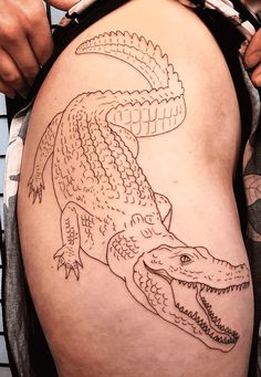 a man with a tattoo on his thigh holding onto an alligator's head and tail