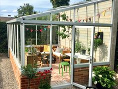 a small greenhouse with plants and flowers in the garden next to some brick walling