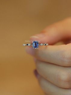 a woman's hand holding an engagement ring with a blue stone in the middle