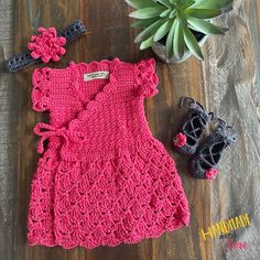 a pink crocheted dress and shoes on a wooden floor next to a succulent plant