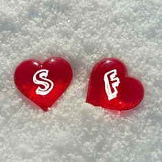 two red heart shaped candys sitting on top of snow covered ground with the letter f