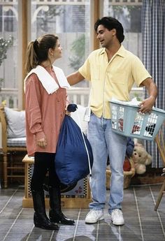 a man and woman standing in a living room with a basket full of stuff on the floor