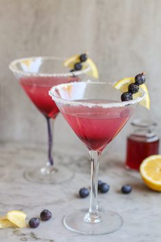 two martinis with blueberries and lemon garnish sit on a marble table