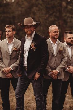 a group of men standing next to each other in front of trees wearing suits and hats