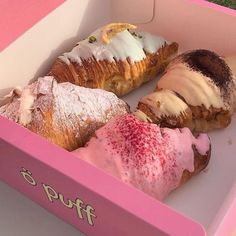 four pastries are in a pink box on the grass, and one is covered with powdered sugar