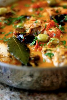 a close up of a bowl of soup with olives, tomatoes and other vegetables